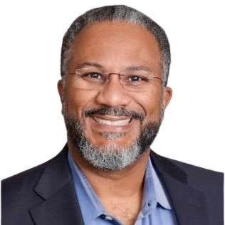 Smiling man with a gray beard and glasses, wearing a blue shirt and dark blazer.