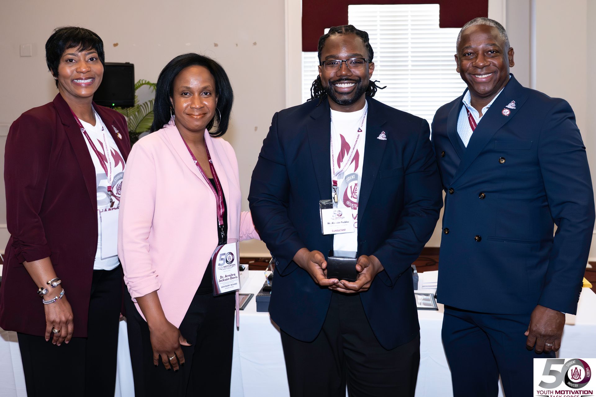 Four people posing at an event. Man in center holds an award. Others wear lanyards and business attire.