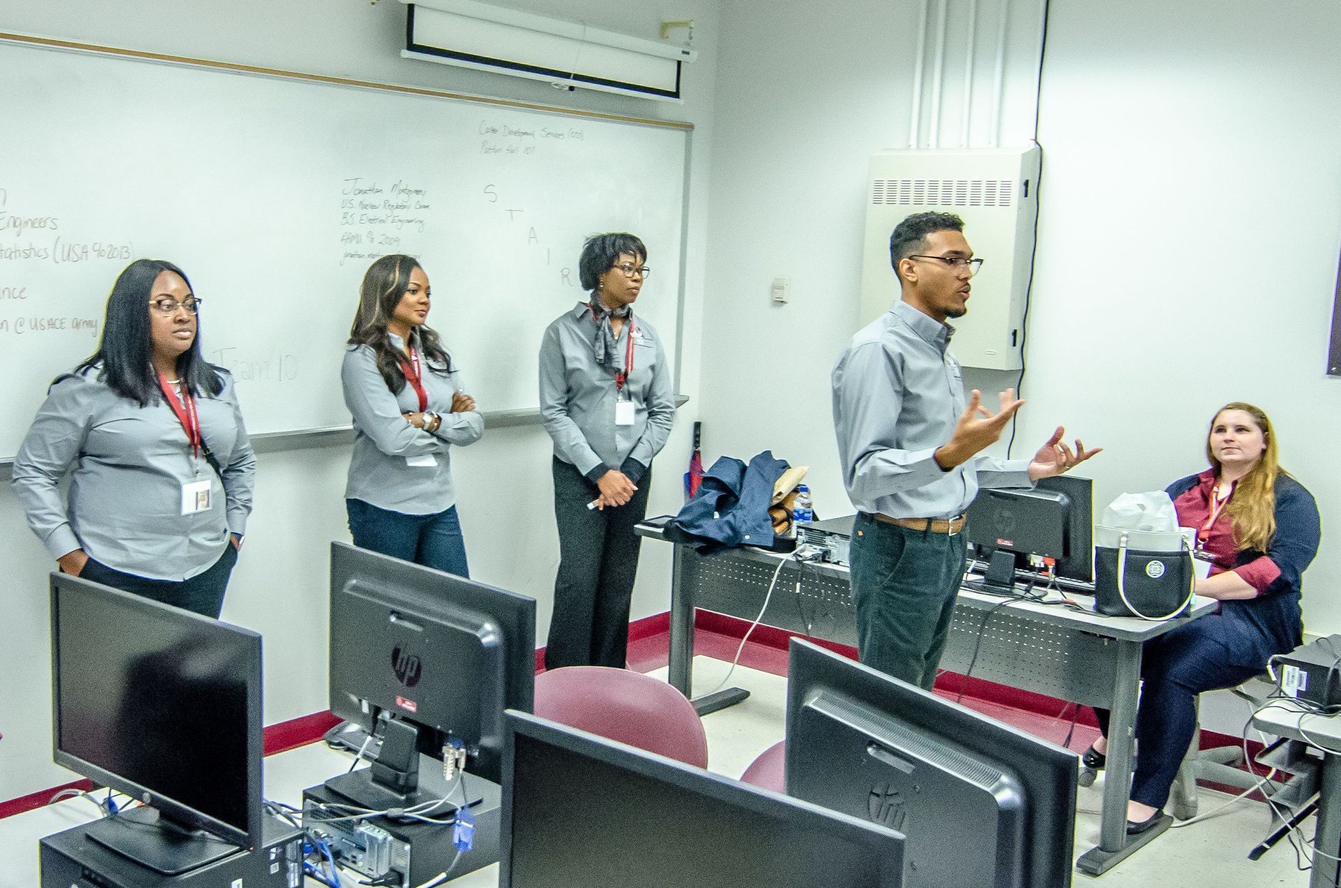People in a classroom setting, one person speaking, others listening, computers in front.