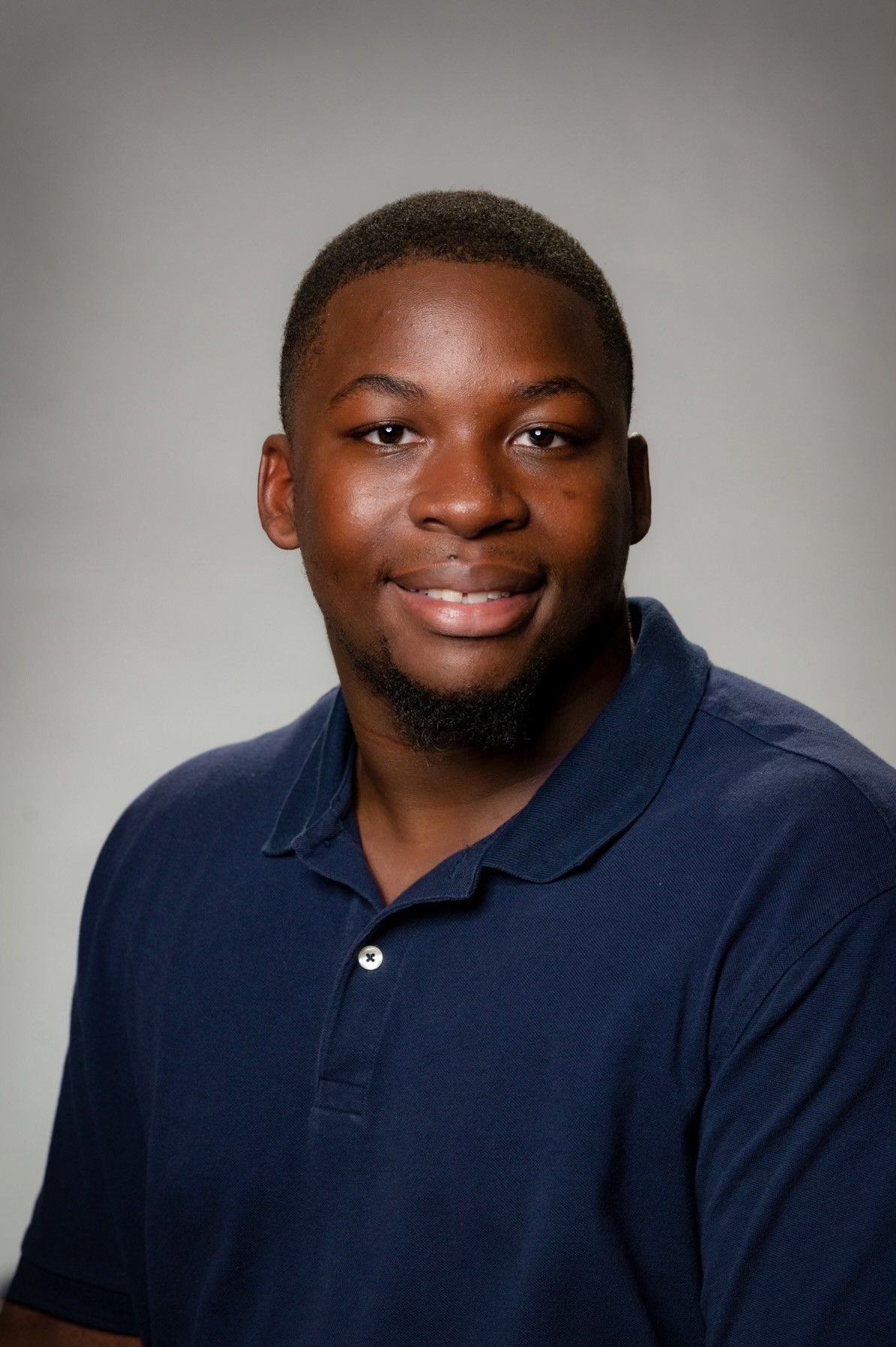 Man in a blue polo shirt smiles; plain gray background.