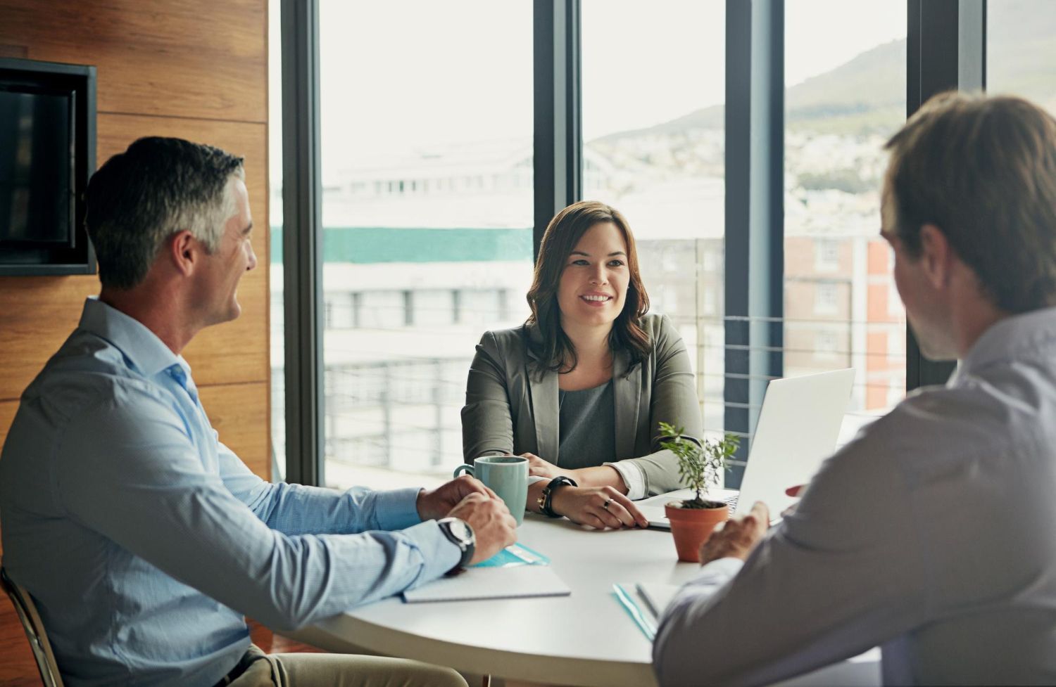 Three people in a bright conference room meeting around a table.