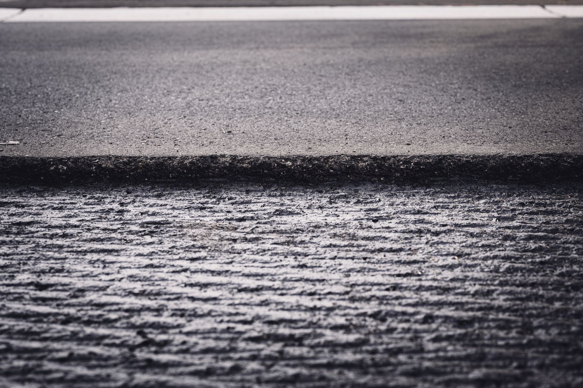 Close-up of a road surface showing a smooth section next to a rough, milled asphalt strip.