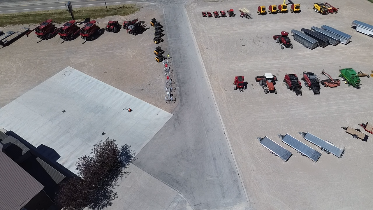 Aerial view of a lot filled with parked farm machinery, combines, and trailers.