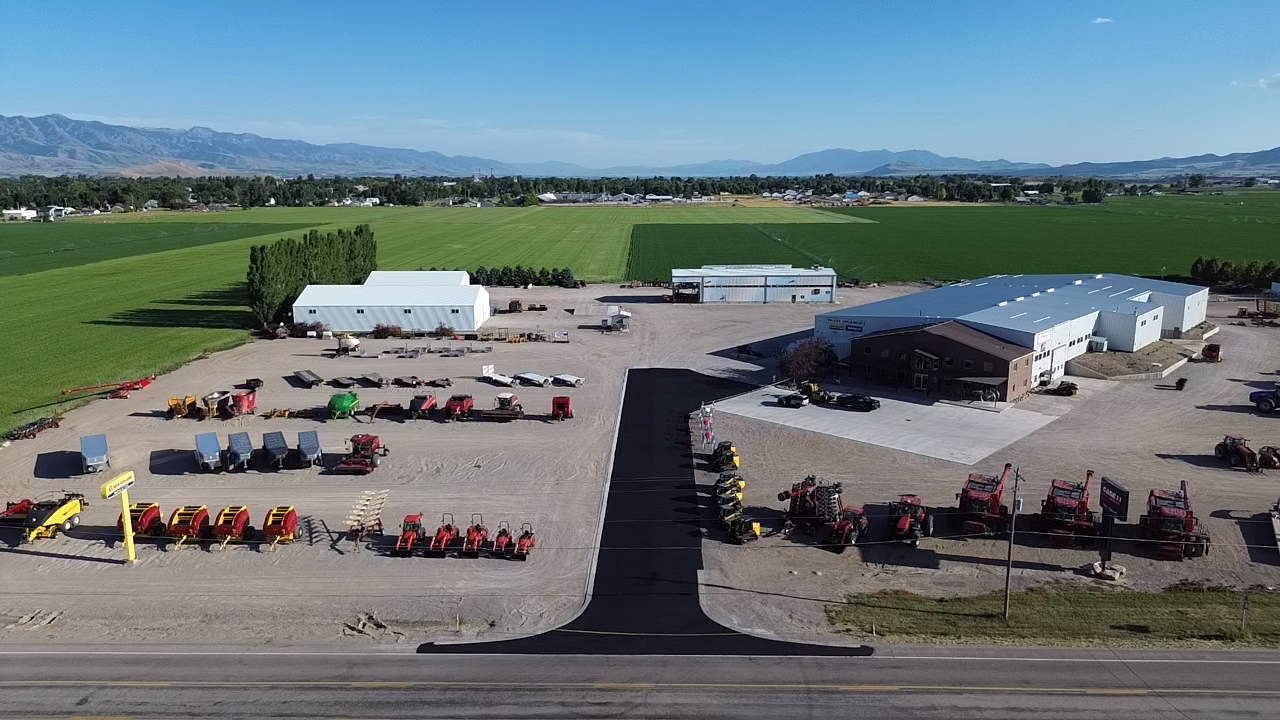 Aerial view of an agricultural equipment dealership with machinery rows, buildings, and surrounding fields.