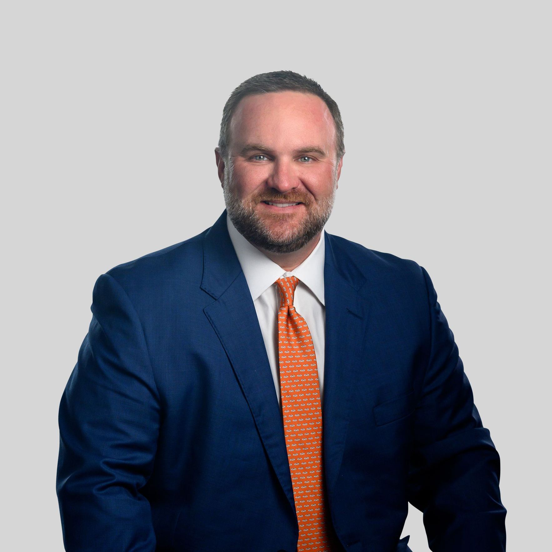 Portrait of a man in a navy suit with an orange tie against a light gray background