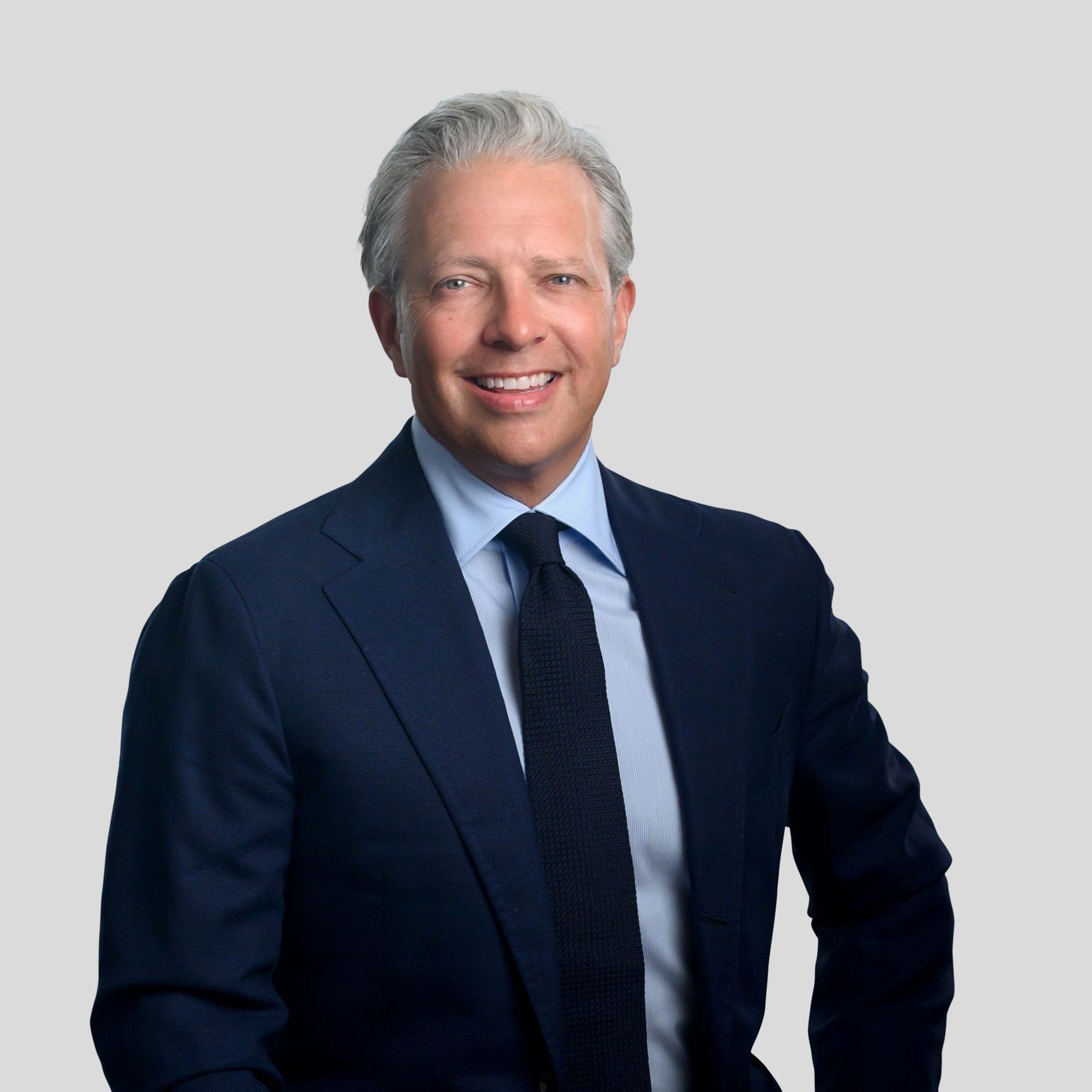 Smiling man in a navy suit against a light gray background
