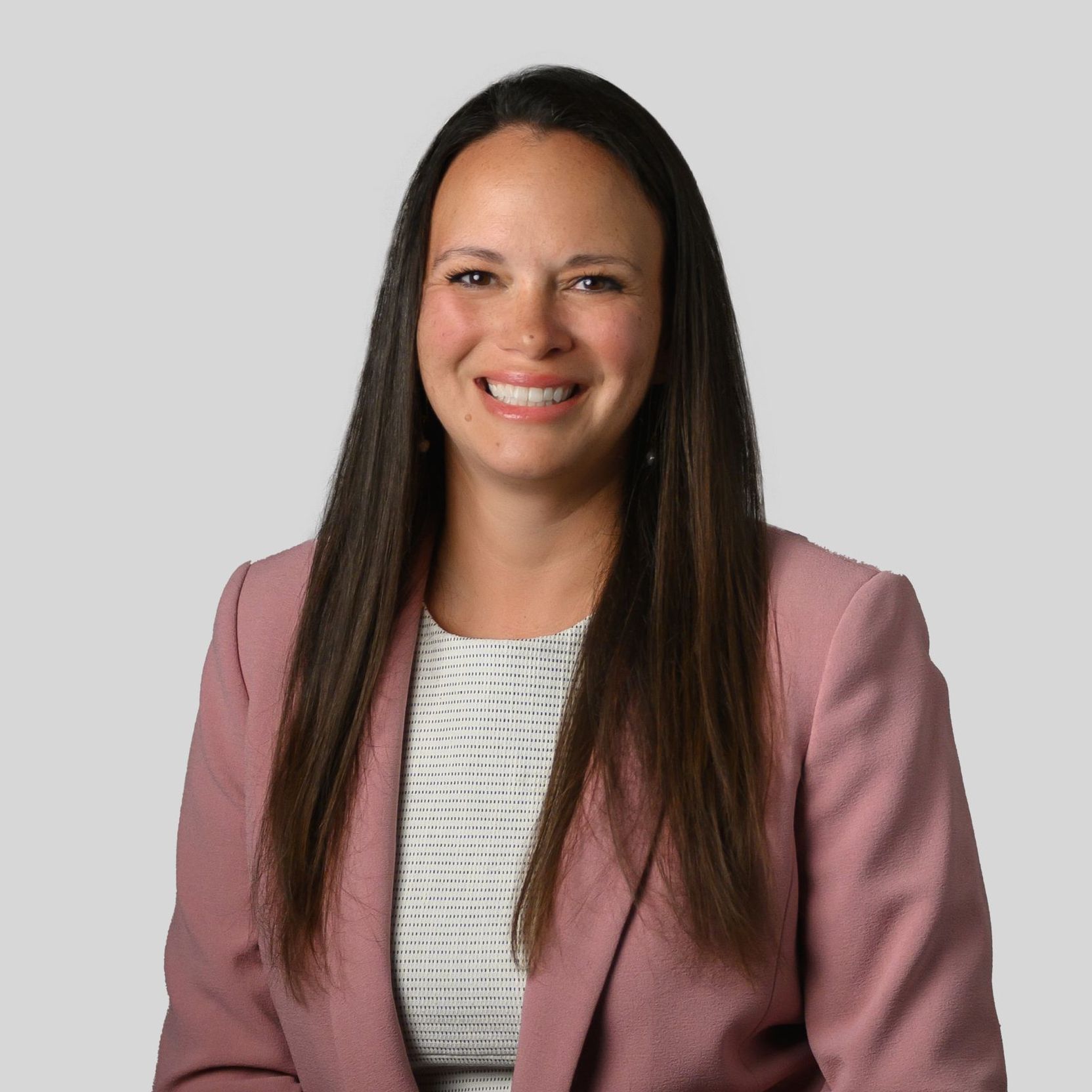 Smiling professional in a pink blazer against a gray background