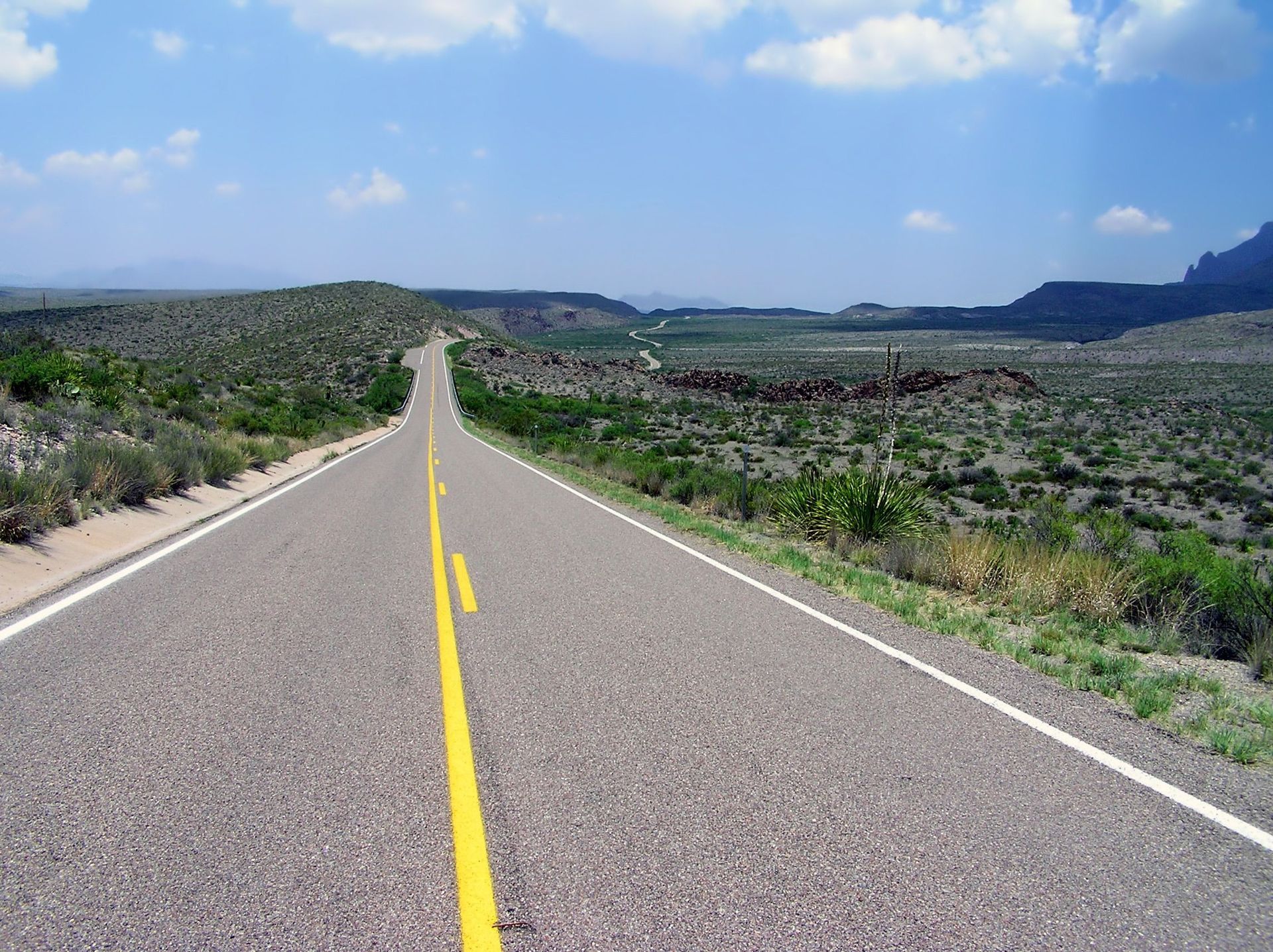 Empty road stretching through a rocky desert landscape under a blue sky with clouds