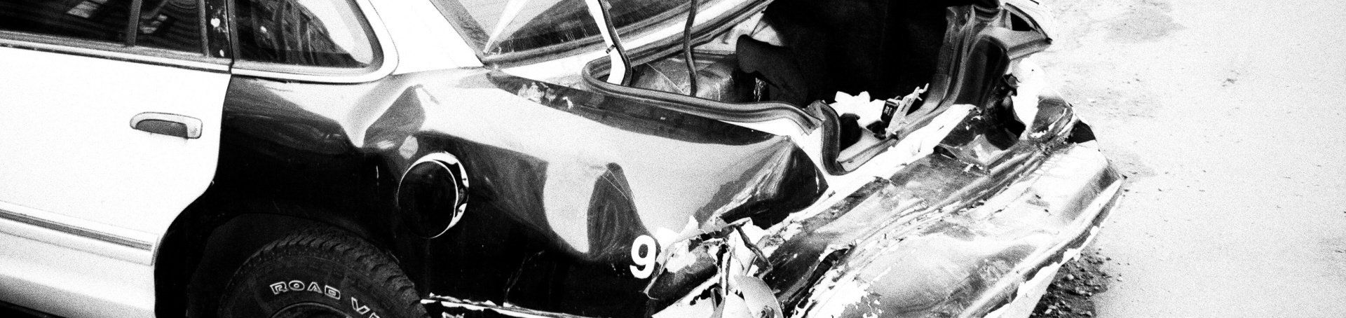 Severe front-end car crash with twisted metal and damaged bumper in black and white.