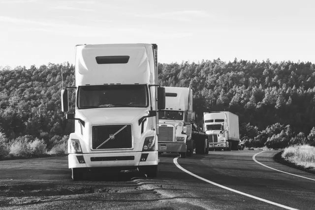 Three semi trucks driving along a curving road past trees