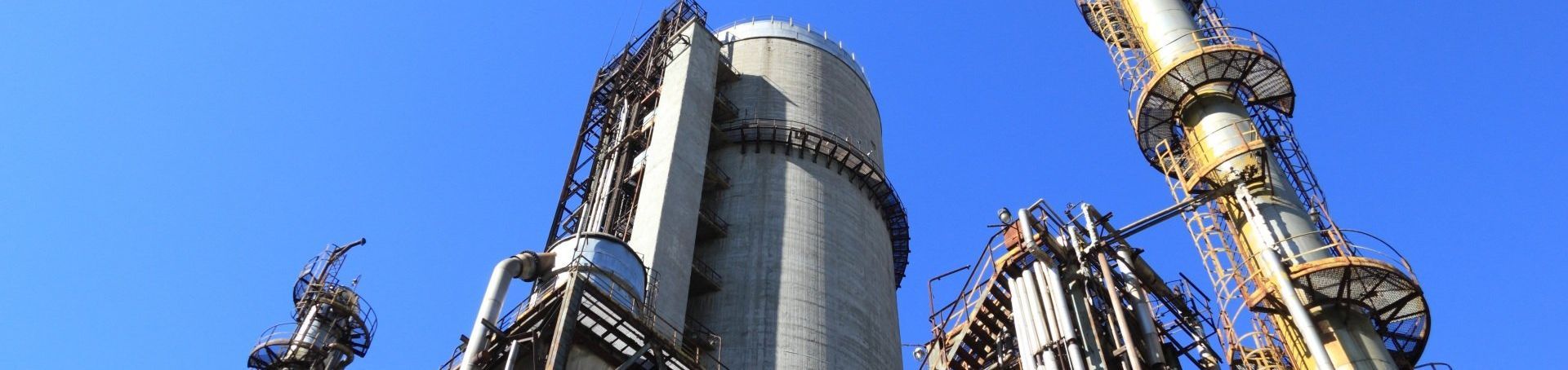 Silver industrial towers and yellow piping against a clear blue sky