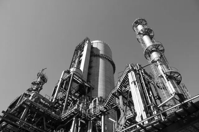 Black-and-white industrial refinery towers and pipes against the sky