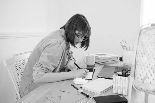 Person working at a desk with a laptop, notebook, and coffee in a bright room