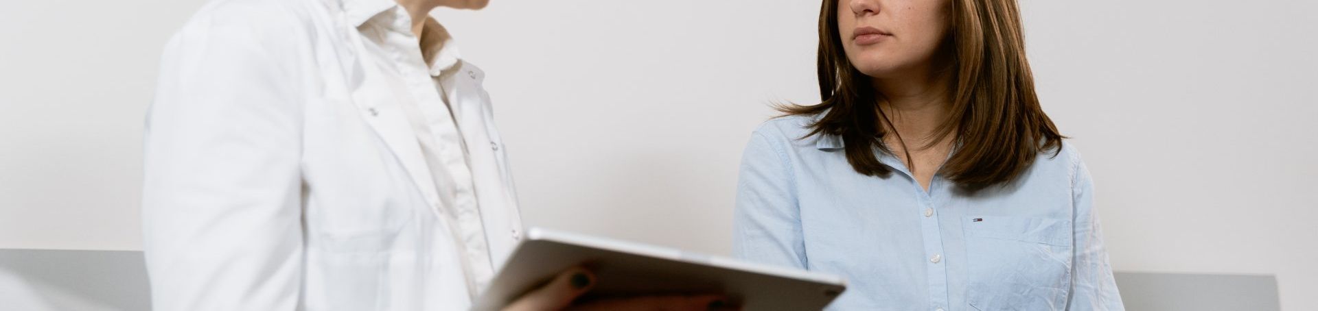 Two people in a bright office discussing a laptop, one in a white coat and one in a blue shirt