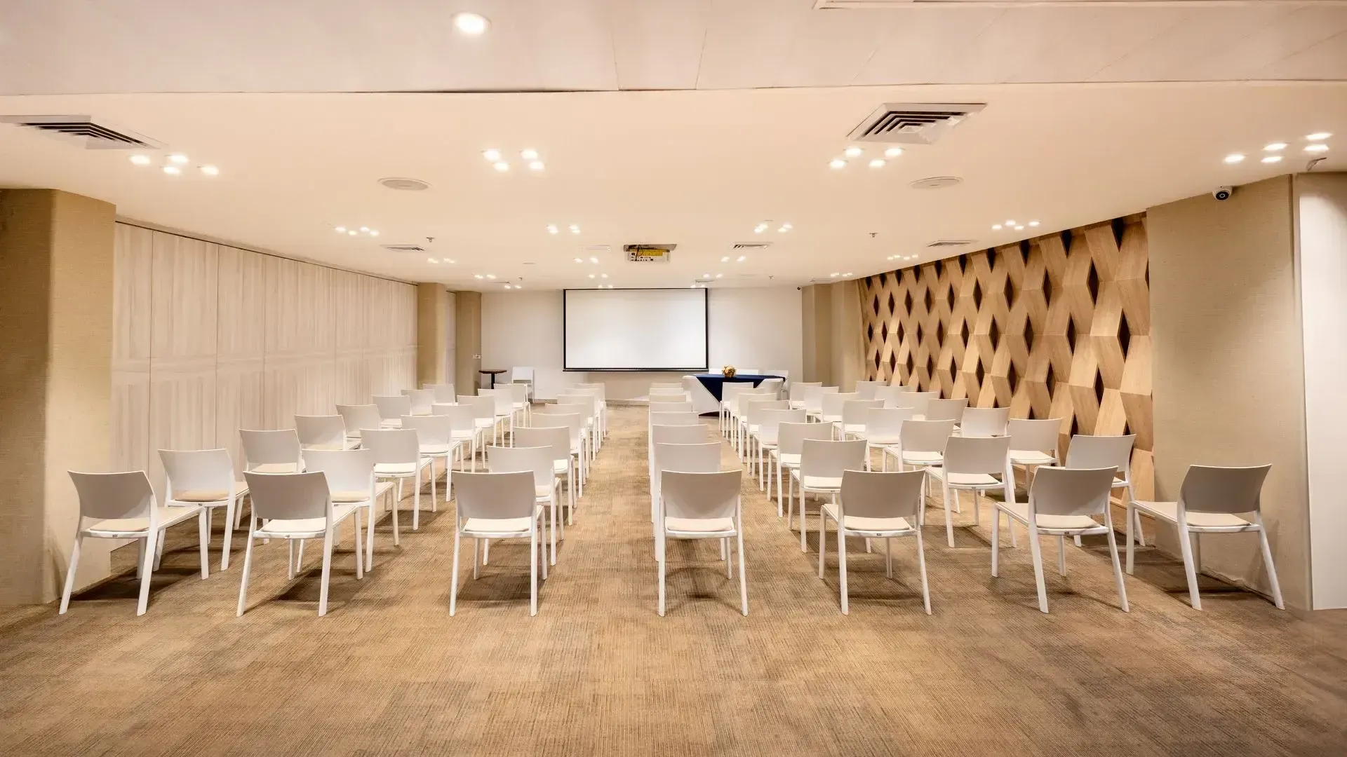 salon de eventos san andres con sillas blancas, pantalla de proyección y pared decorativa de madera
