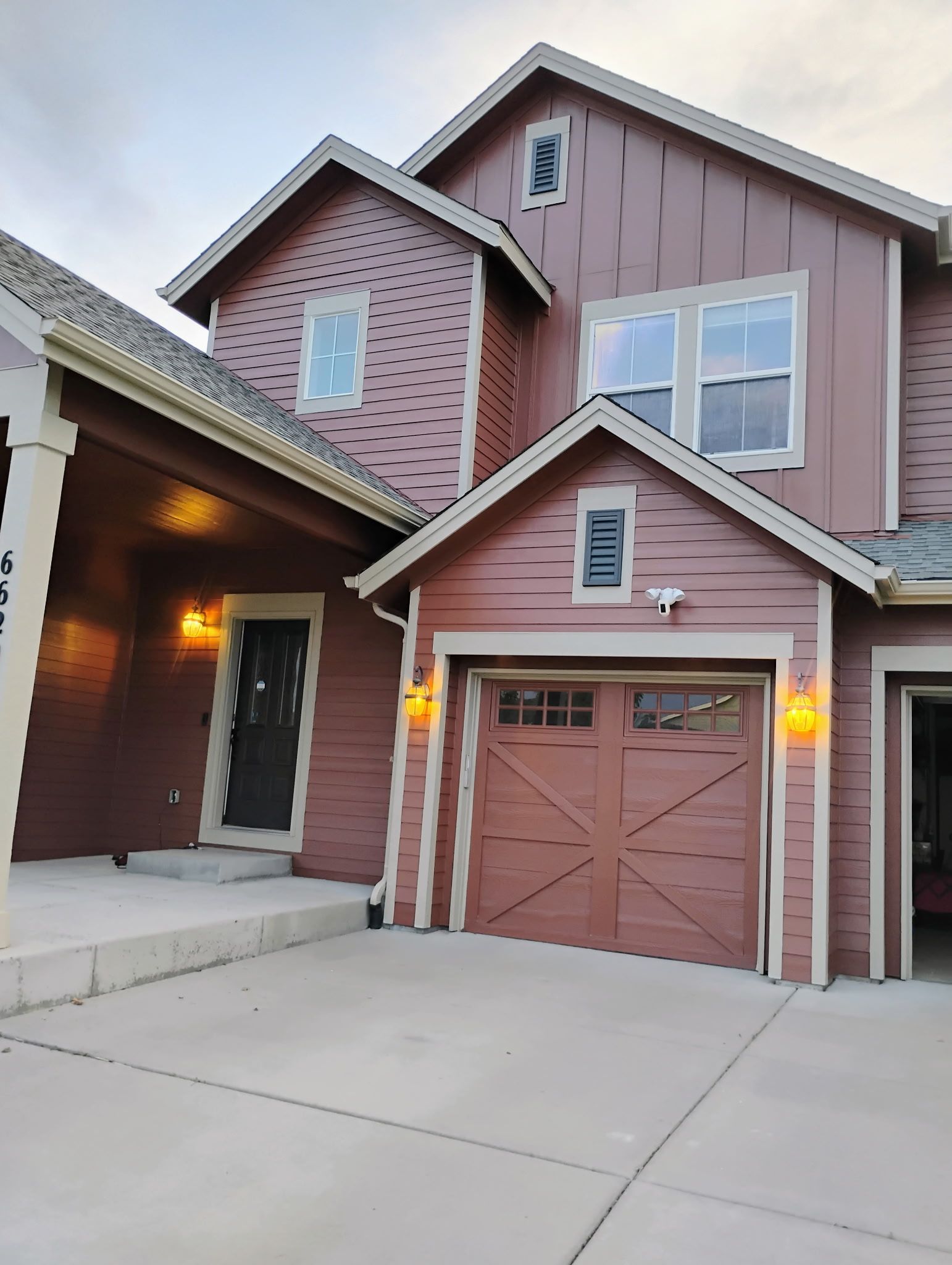 Suburban townhouse exterior with pink siding, a garage, and a front porch at dusk
