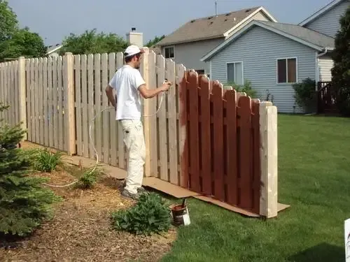 Person staining a wooden fence in a suburban backyard.