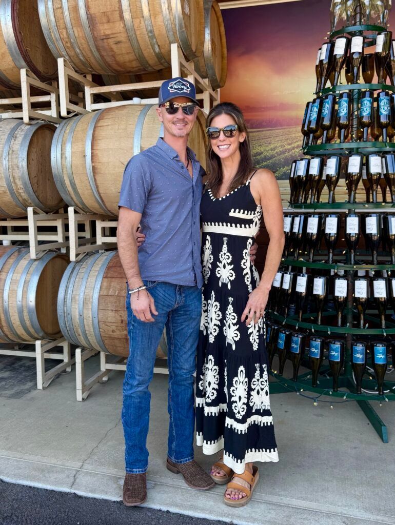 Couple posing beside stacked wine barrels and bottles in a winery display