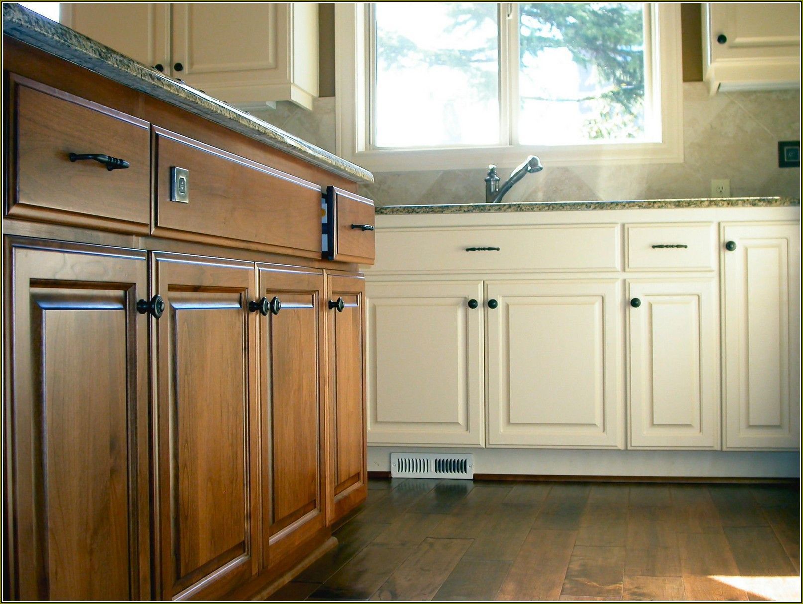 Bright kitchen with wooden and white cabinets, a sink under a window, and dark wood floor.
