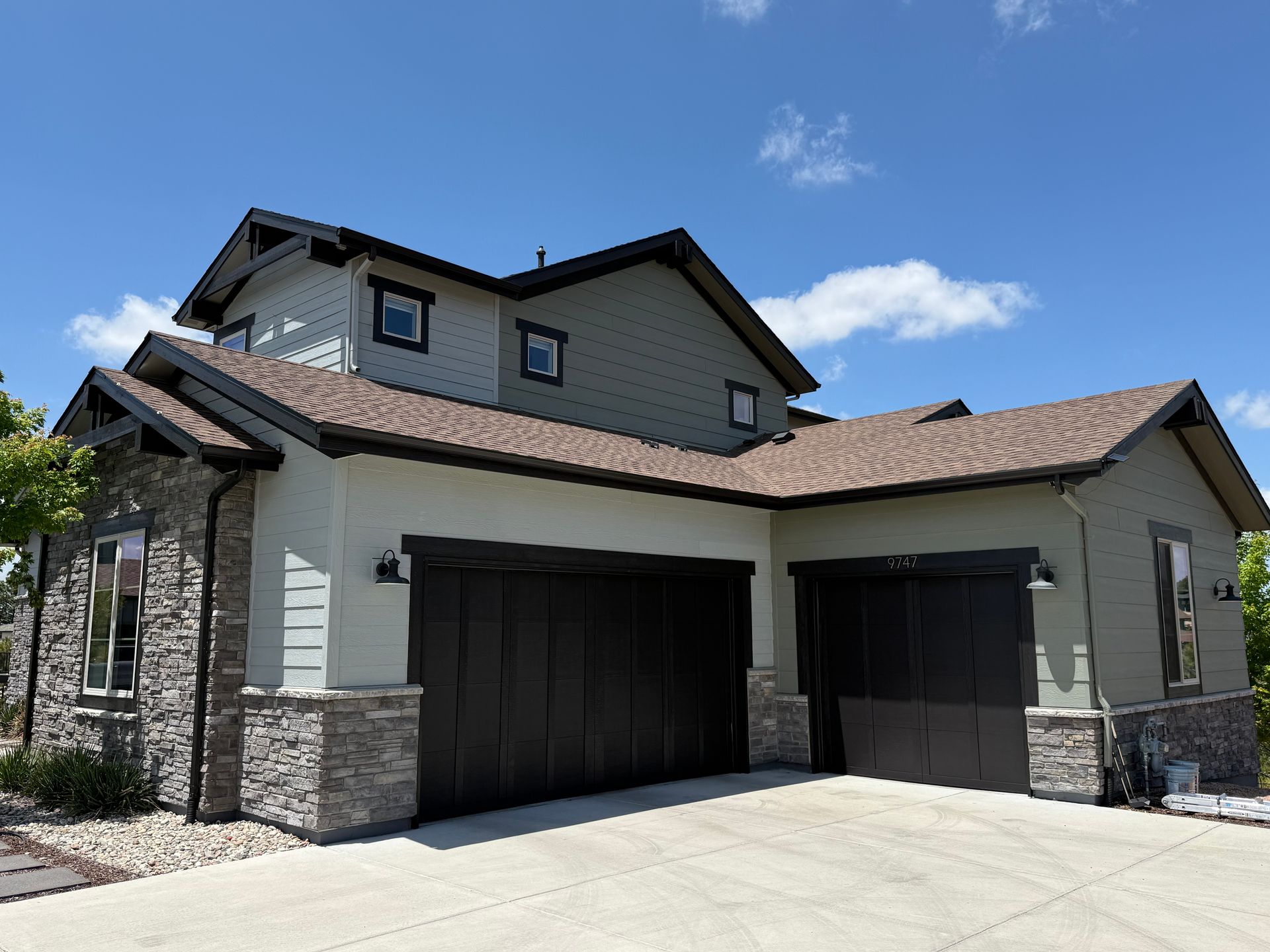 Modern beige and stone suburban house exterior with dark garage doors under a blue sky
