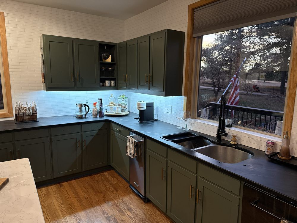Modern kitchen with dark green cabinets, black countertops, and a window over the sink