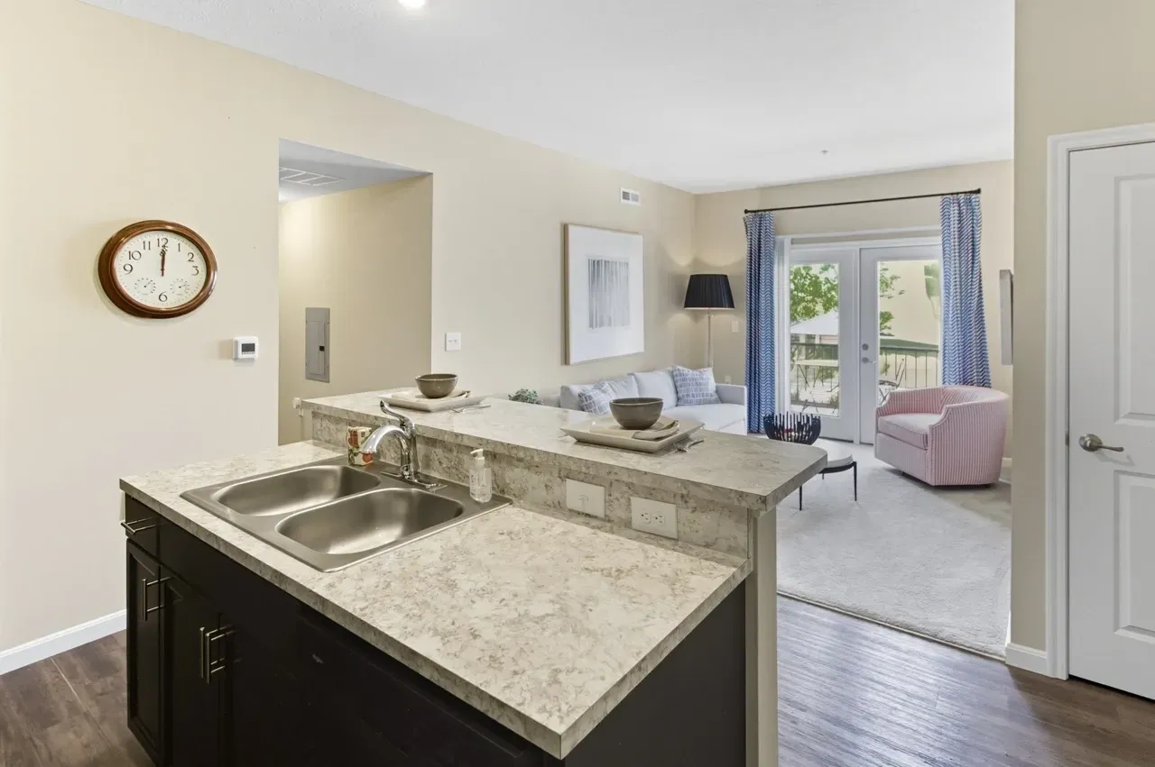 Kitchen island with sink overlooking a living room with a couch, armchair, and balcony access.