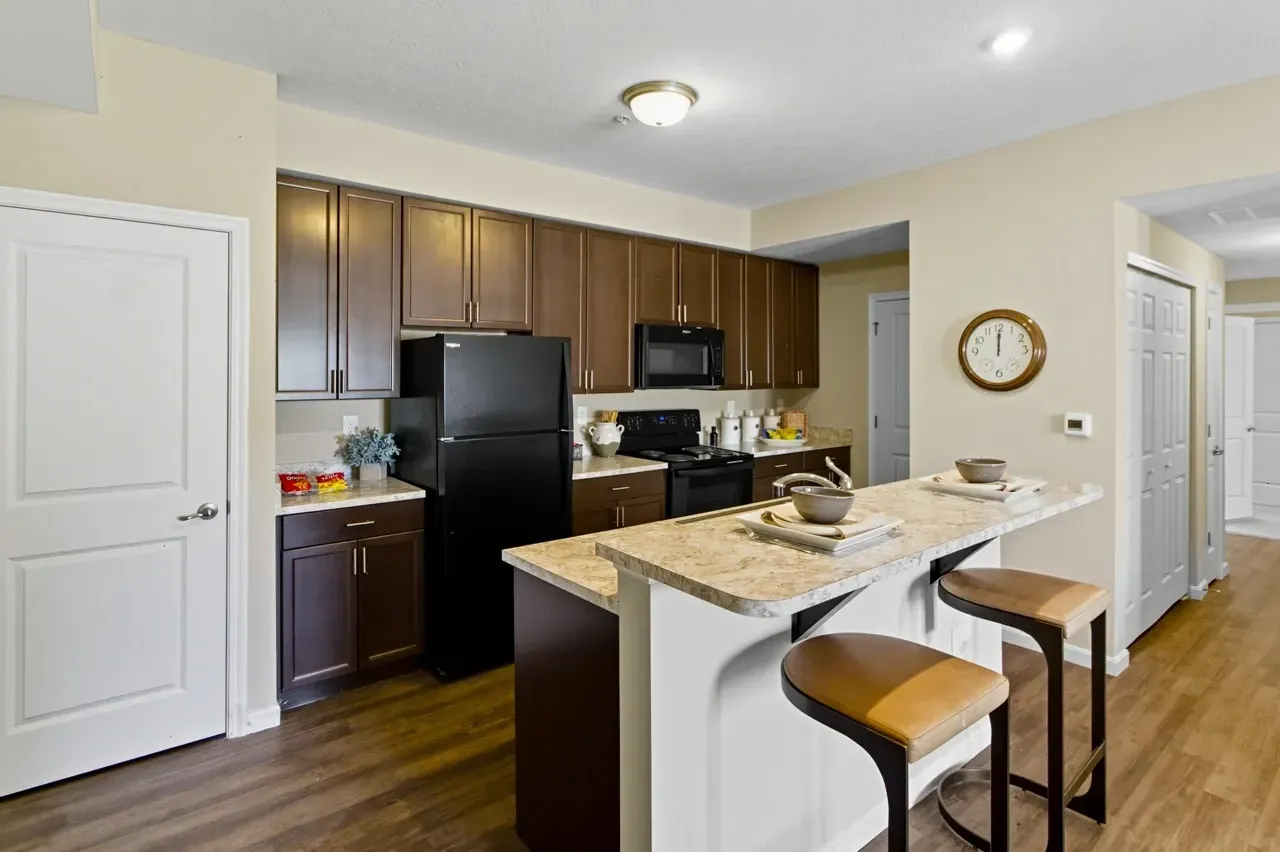 Modern kitchen with dark wood cabinets, black appliances, and a breakfast bar with stools.