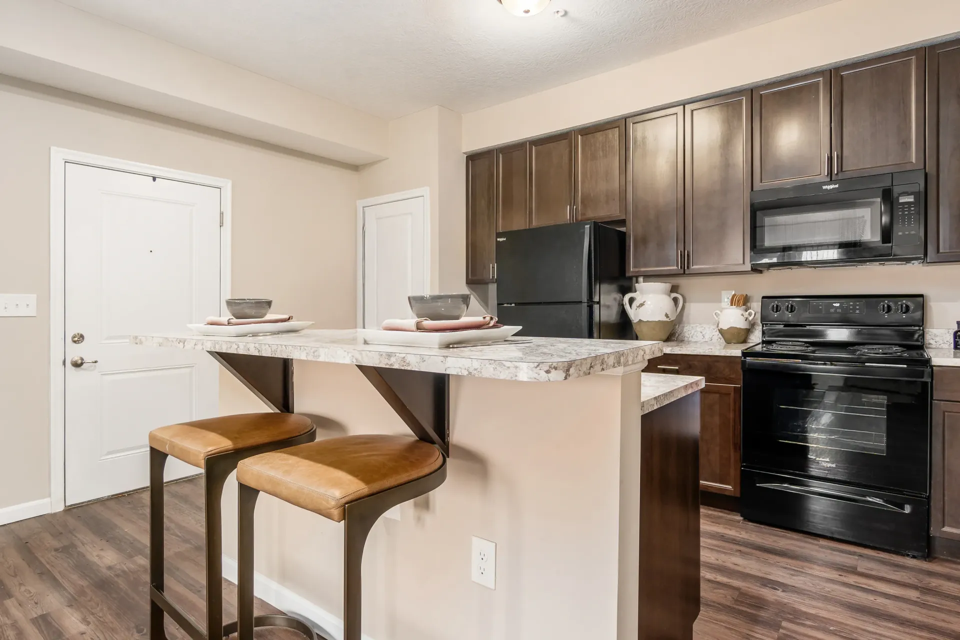 Kitchen island with two bar stools and a view of the kitchen cabinets, refrigerator, and oven.