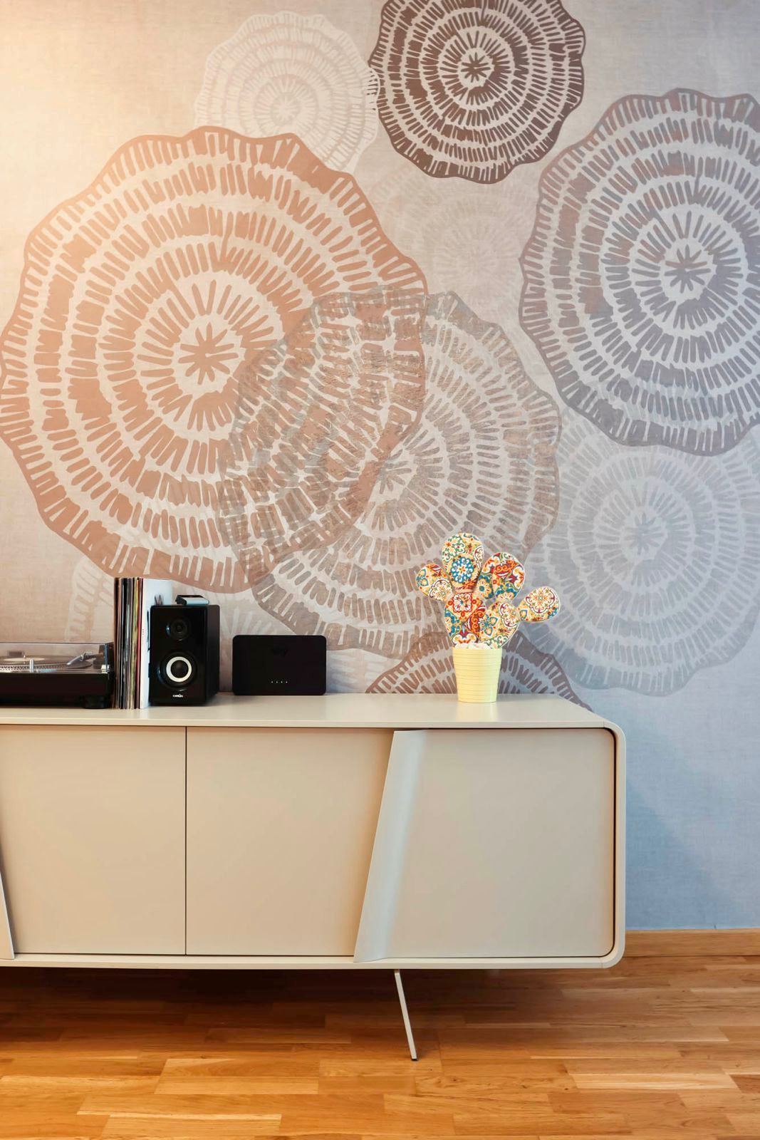 Soggiorno moderno con quadri floreali alle pareti, un mobile basso, impianto stereo e un vaso di fiori su un pavimento in legno.