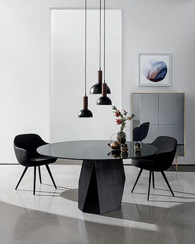 Una moderna sala da pranzo con un tavolo ovale nero, tre lampade a sospensione nere e sedie nere.