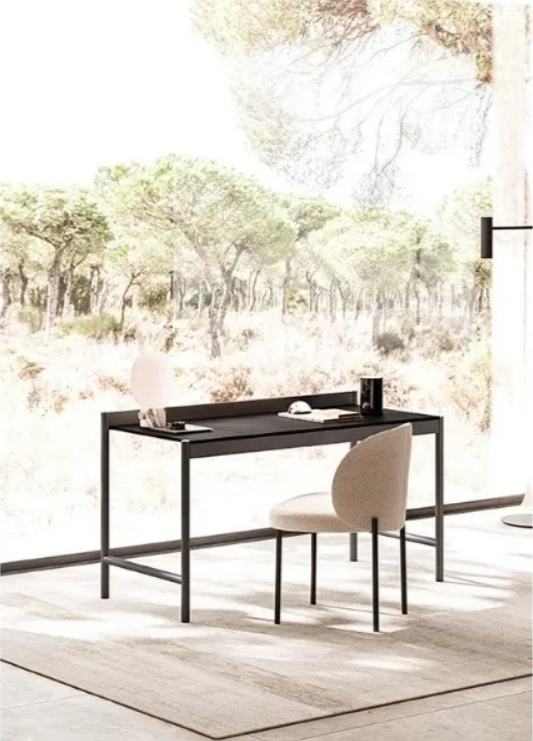 Scrivania con sedia davanti a una finestra con vista sugli alberi. Scrivania nera, sedia beige, tappeto neutro, vista esterna luminosa.
