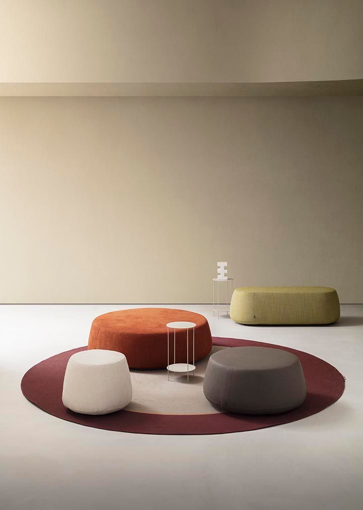 Stanza con pouf arancioni, bianchi e grigi su un tappeto rotondo; pouf verde oliva sullo sfondo.