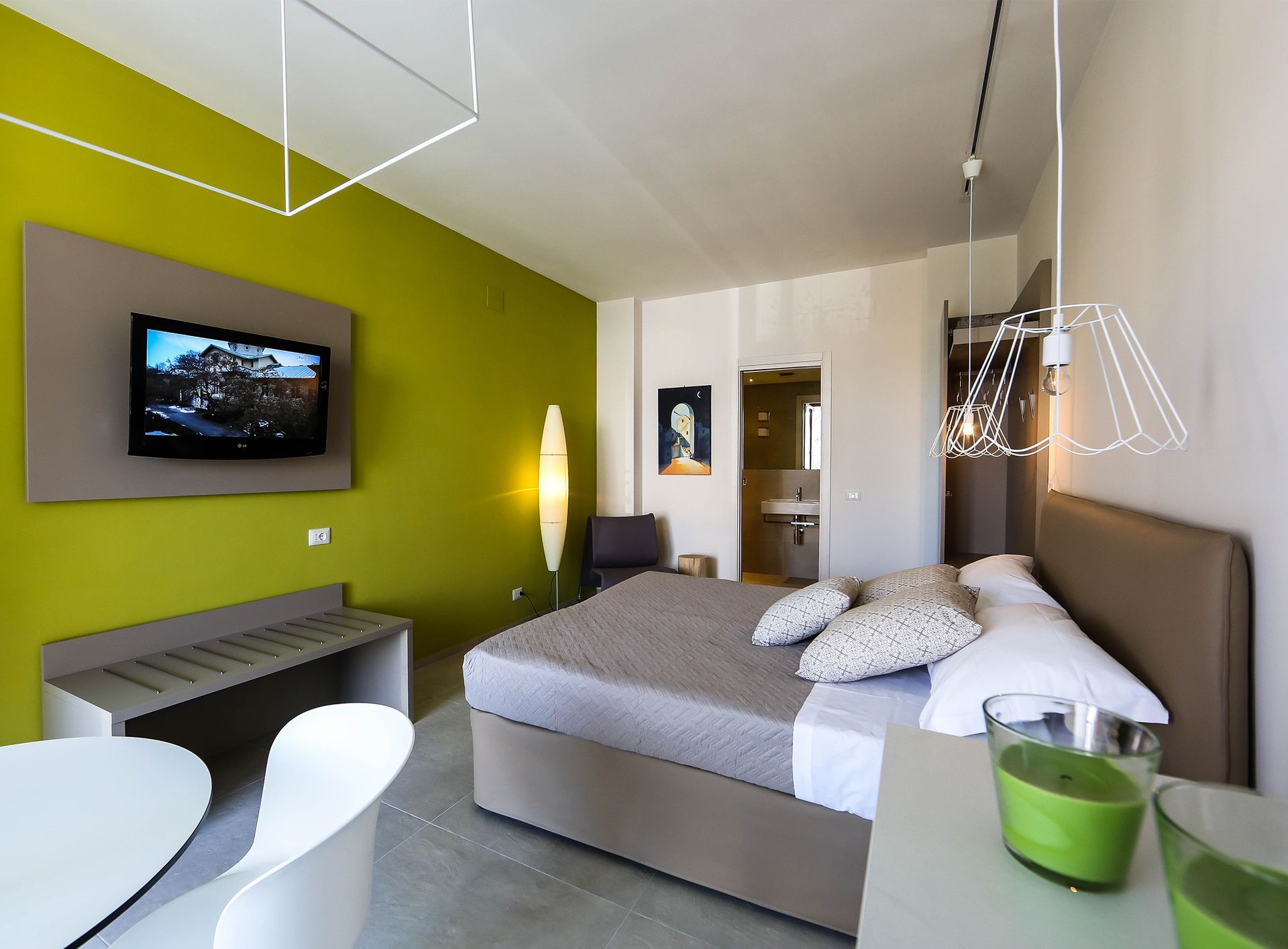 Camera da letto moderna con parete verde lime, TV a parete, letto e sedie bianche vicino a una finestra.