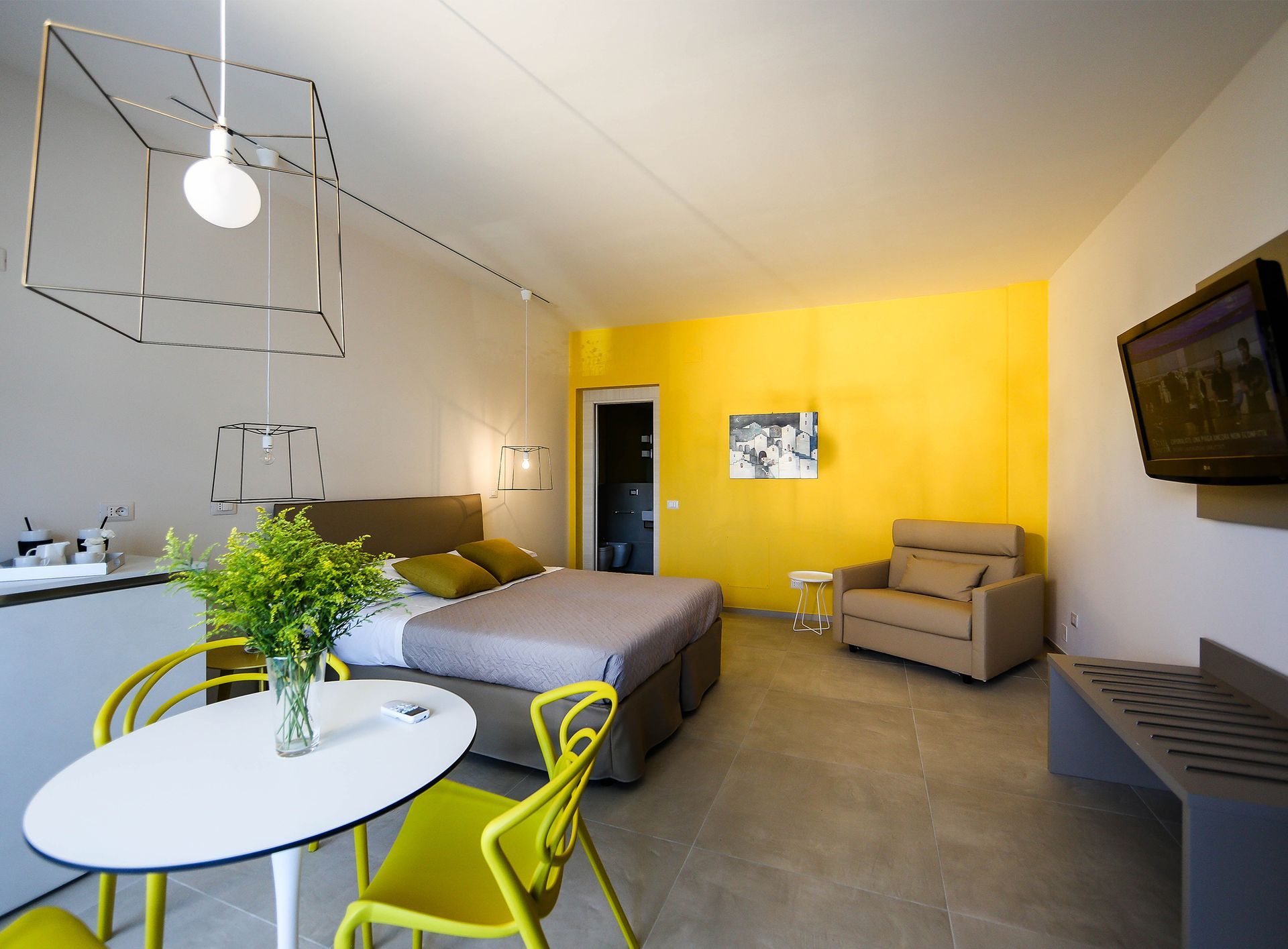Monolocale moderno con letto, divano, tavolo da pranzo, parete decorativa gialla e TV a parete.