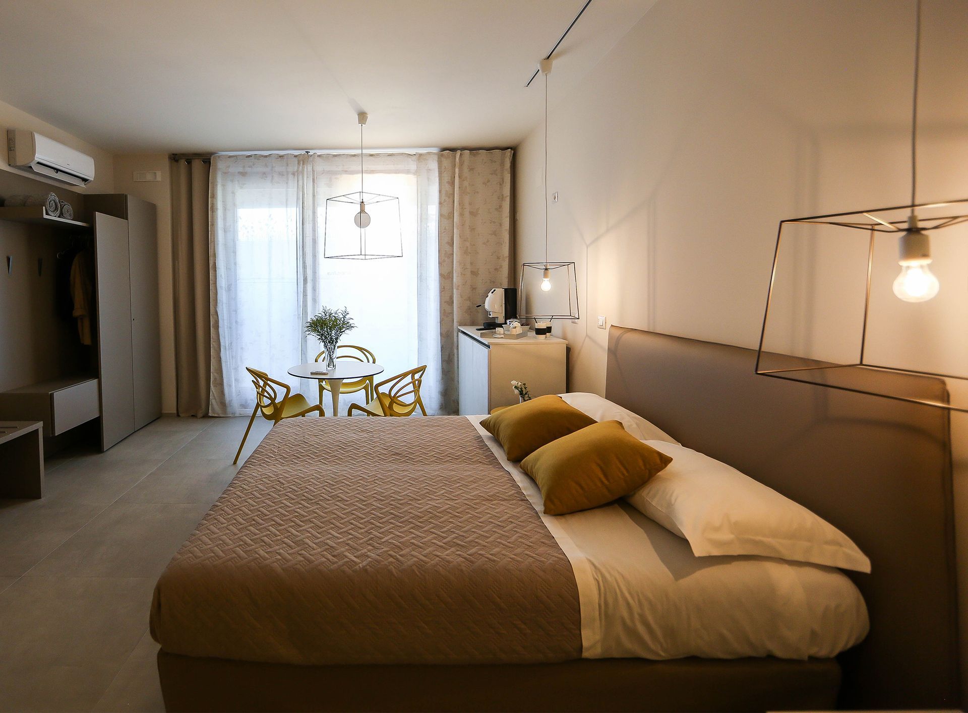Accogliente camera da letto con letto, luci soffuse, scrivania, piante e porte finestre sullo sfondo.