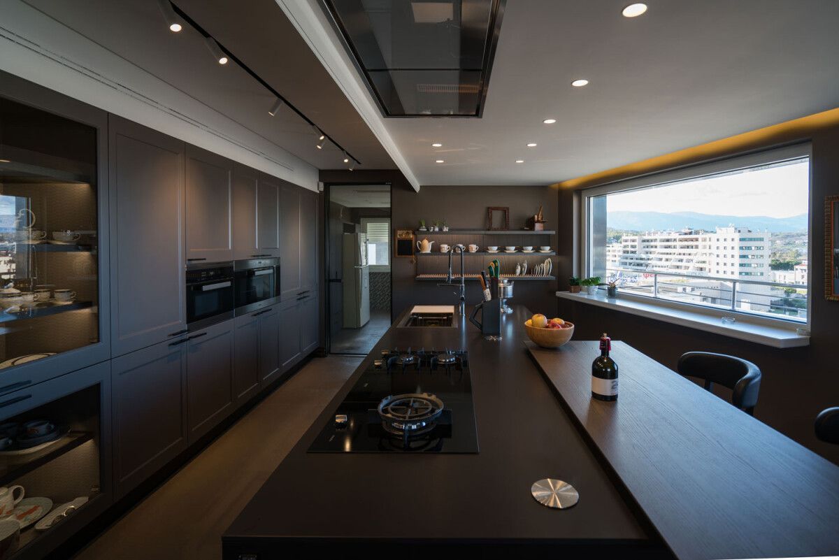 Cucina moderna con mobili scuri, isola lunga e vista sulla città.