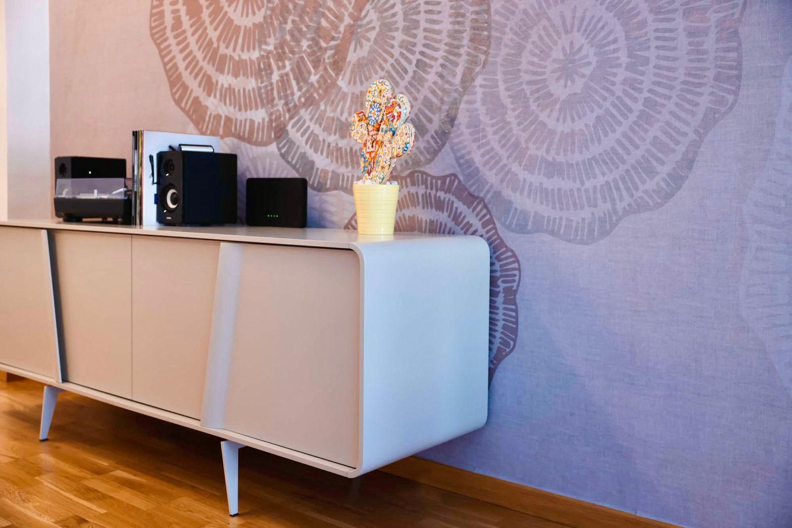 Credenza moderna bianca con stereo nero e un vaso su una parete decorata in una stanza con pavimento in legno.