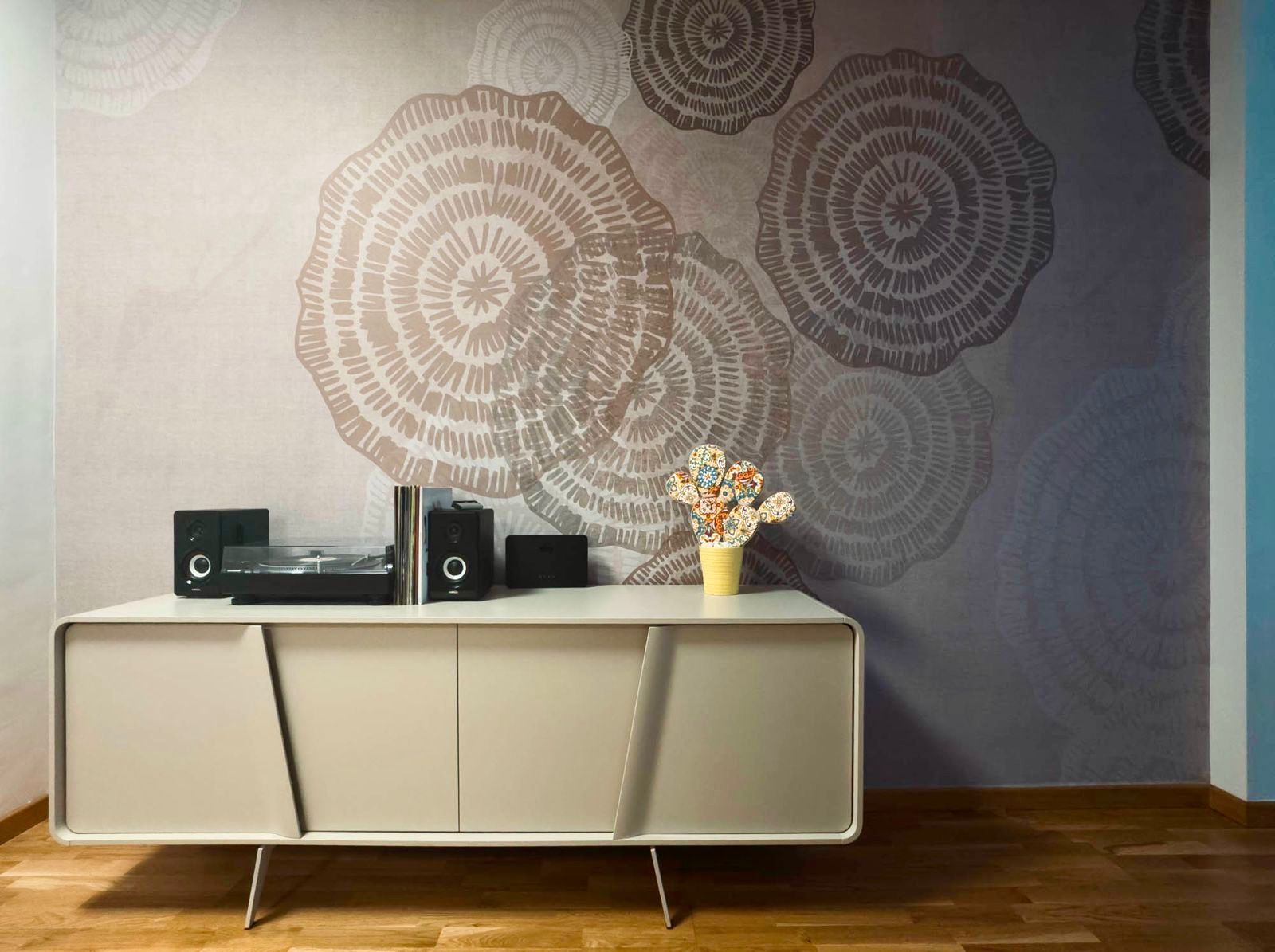 Credenza moderna con altoparlanti stereo e un vaso di fiori contro una parete decorata in un soggiorno.
