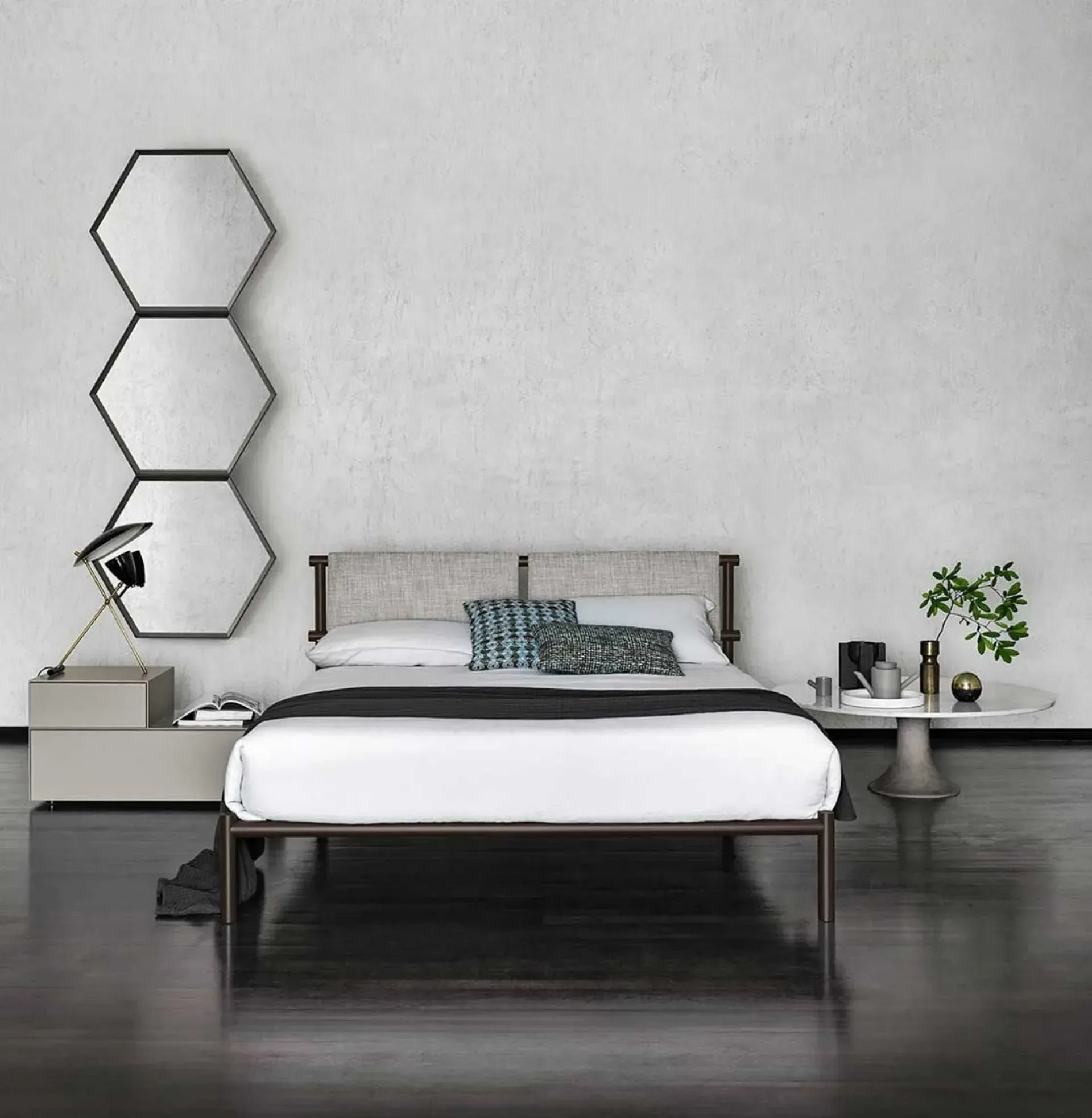 Camera da letto con letto, comodini, specchi decorativi, piante e pavimento nero contro una parete bianca.