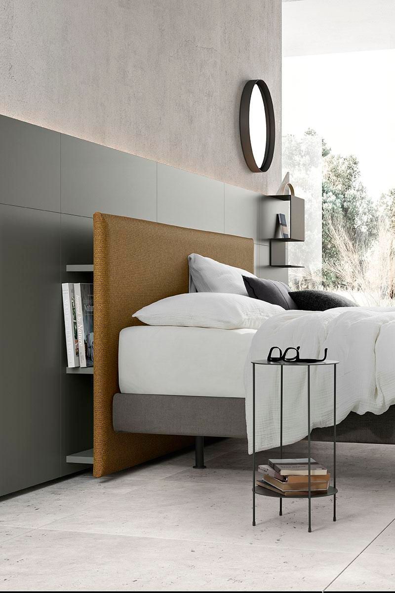 Camera da letto con testiera imbottita, scaffali integrati, tavolino laterale e arredamento moderno.