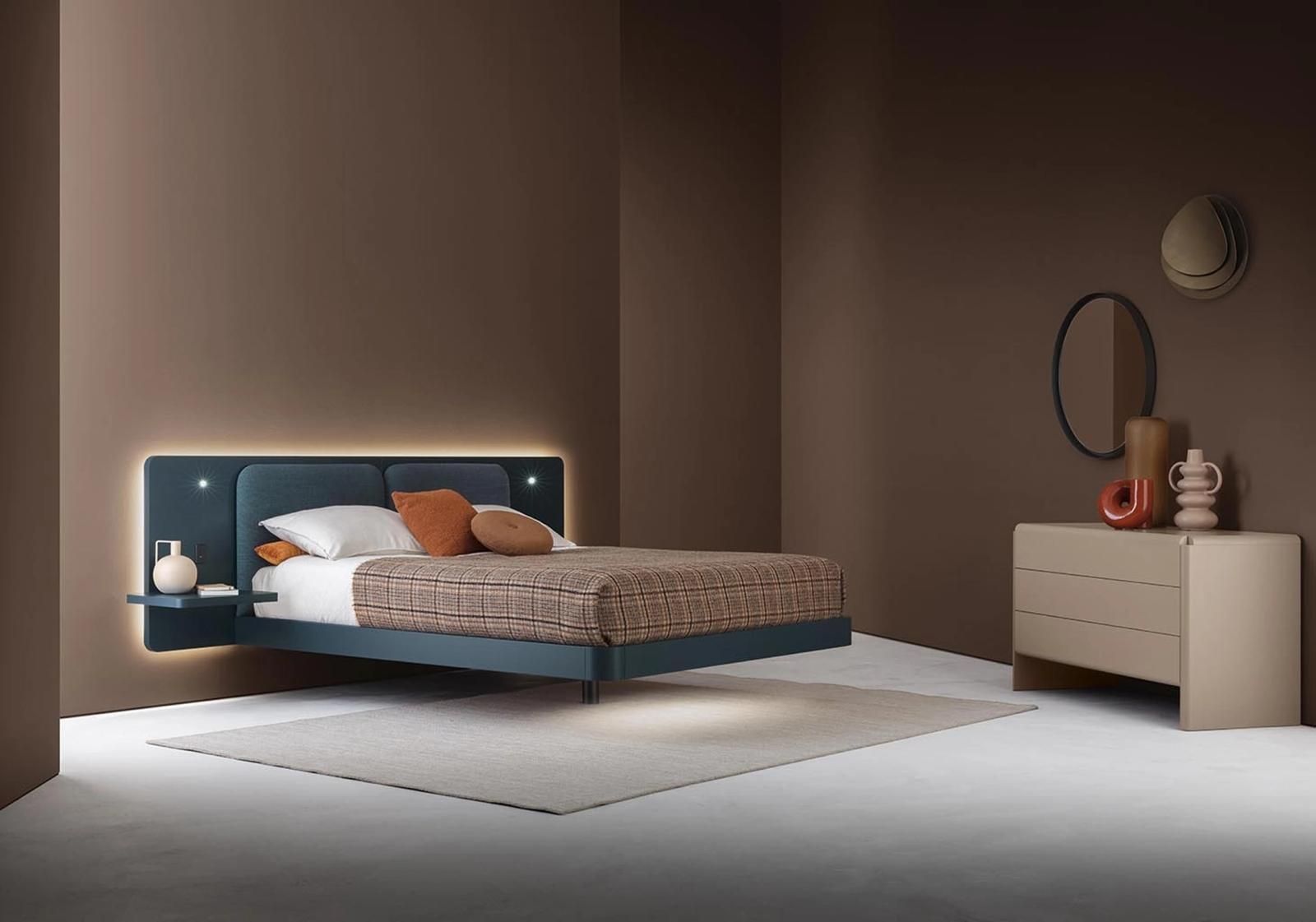 Camera da letto moderna con letto sospeso, testiera verde acqua con luci, comodino, cassettiera e tappeto. Pareti marroni.