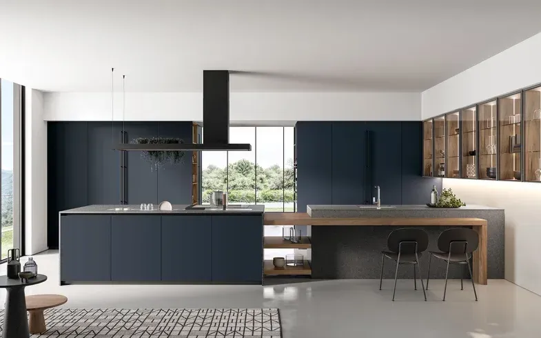 Cucina moderna con mobili blu, isola con piano di lavoro in legno e vetrine in vetro.