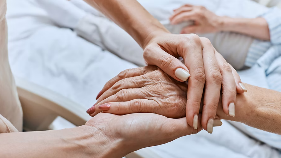 Hands of younger person holding hand of older person, possibly in a hospital setting. We know how to support grief at Reset and Rise Counseling.