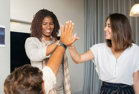 Three people high-fiving in a room, celebrating. Two women and a person with the back to the camera are smiling.