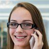 Woman with glasses smiles while talking on a phone.