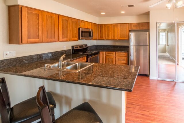 Kitchen with brown cabinets, stainless steel appliances, granite countertop, and bar stools.