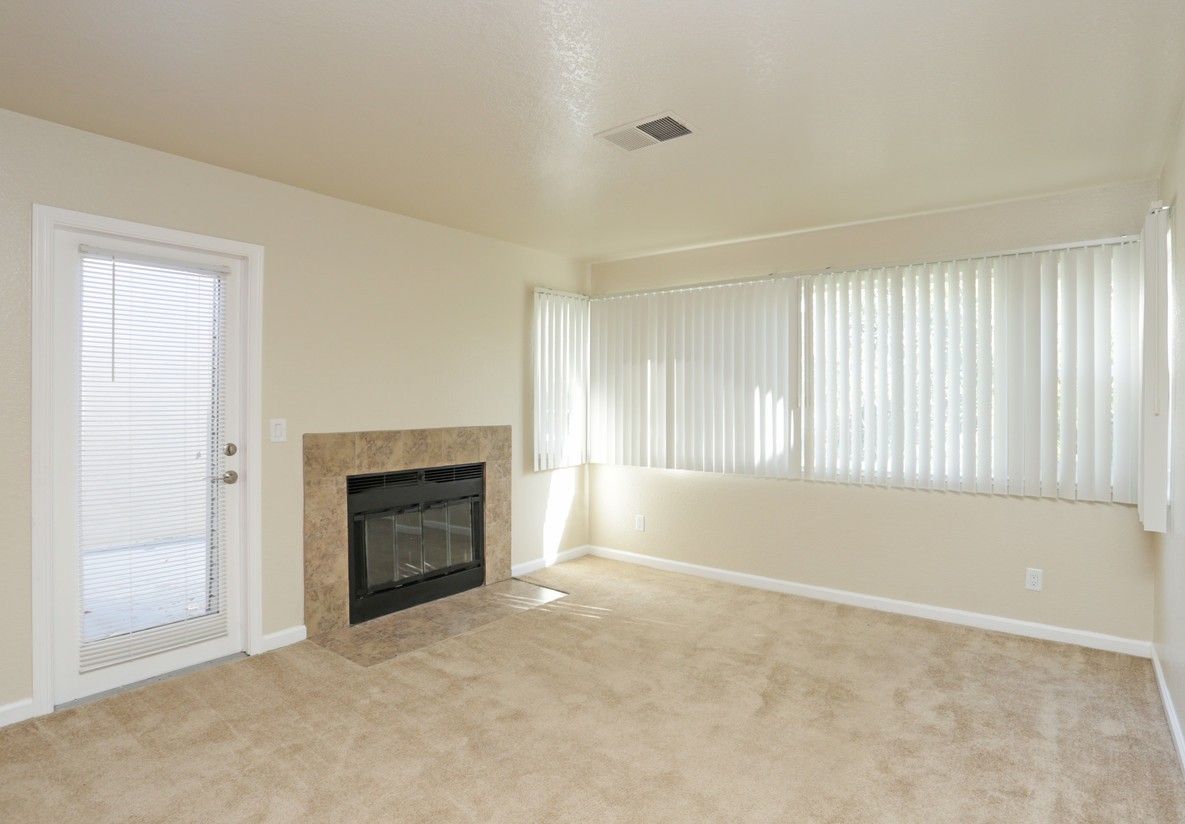 Empty living room with a fireplace, door, and window with blinds.