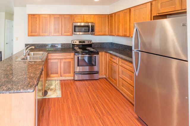 Kitchen with wood cabinets, stainless steel appliances, granite countertops, and wood-look flooring.