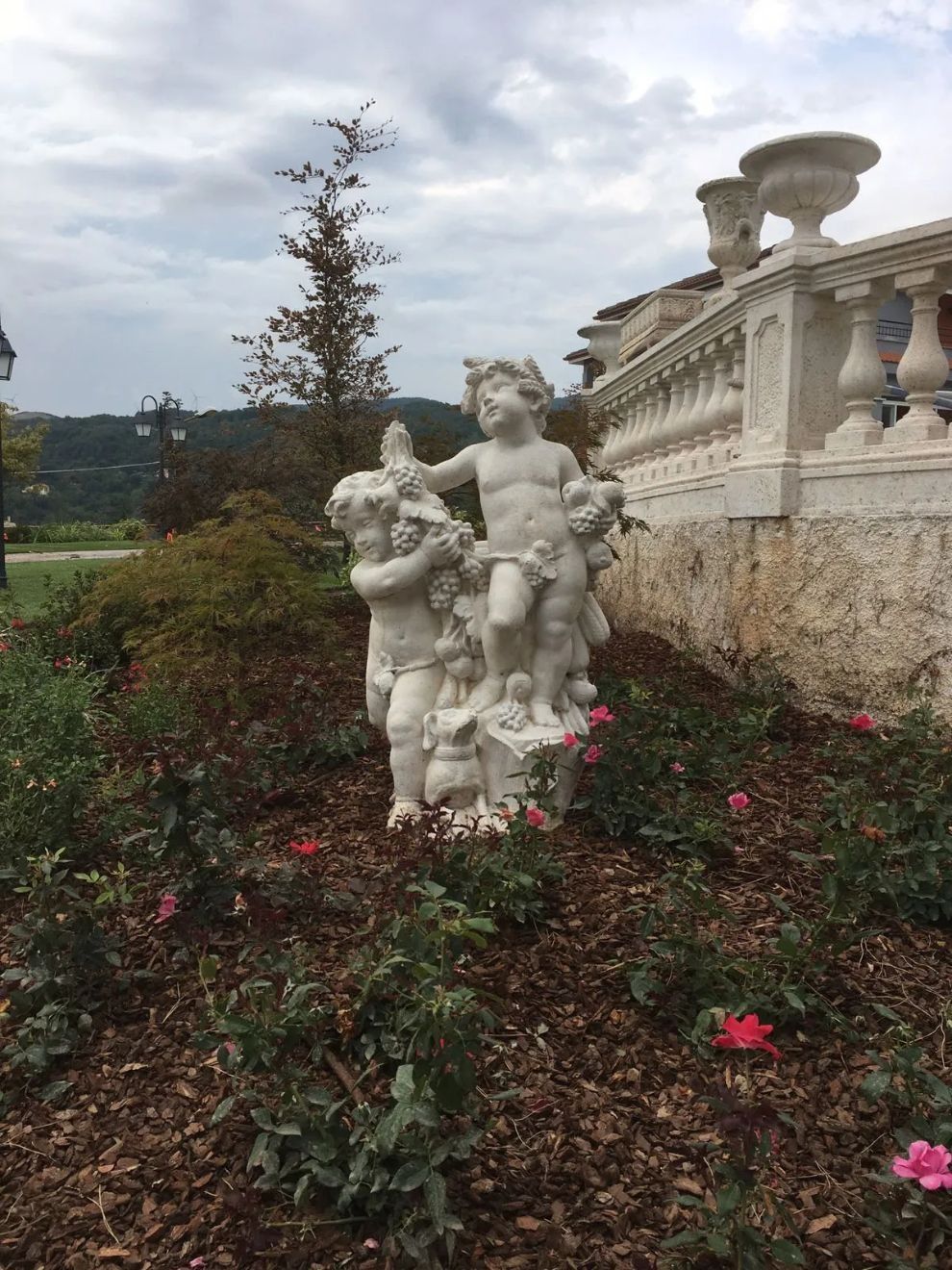 Statue da giardino bianche tra i fiori accanto a una balaustra in pietra in un giardino paesaggistico