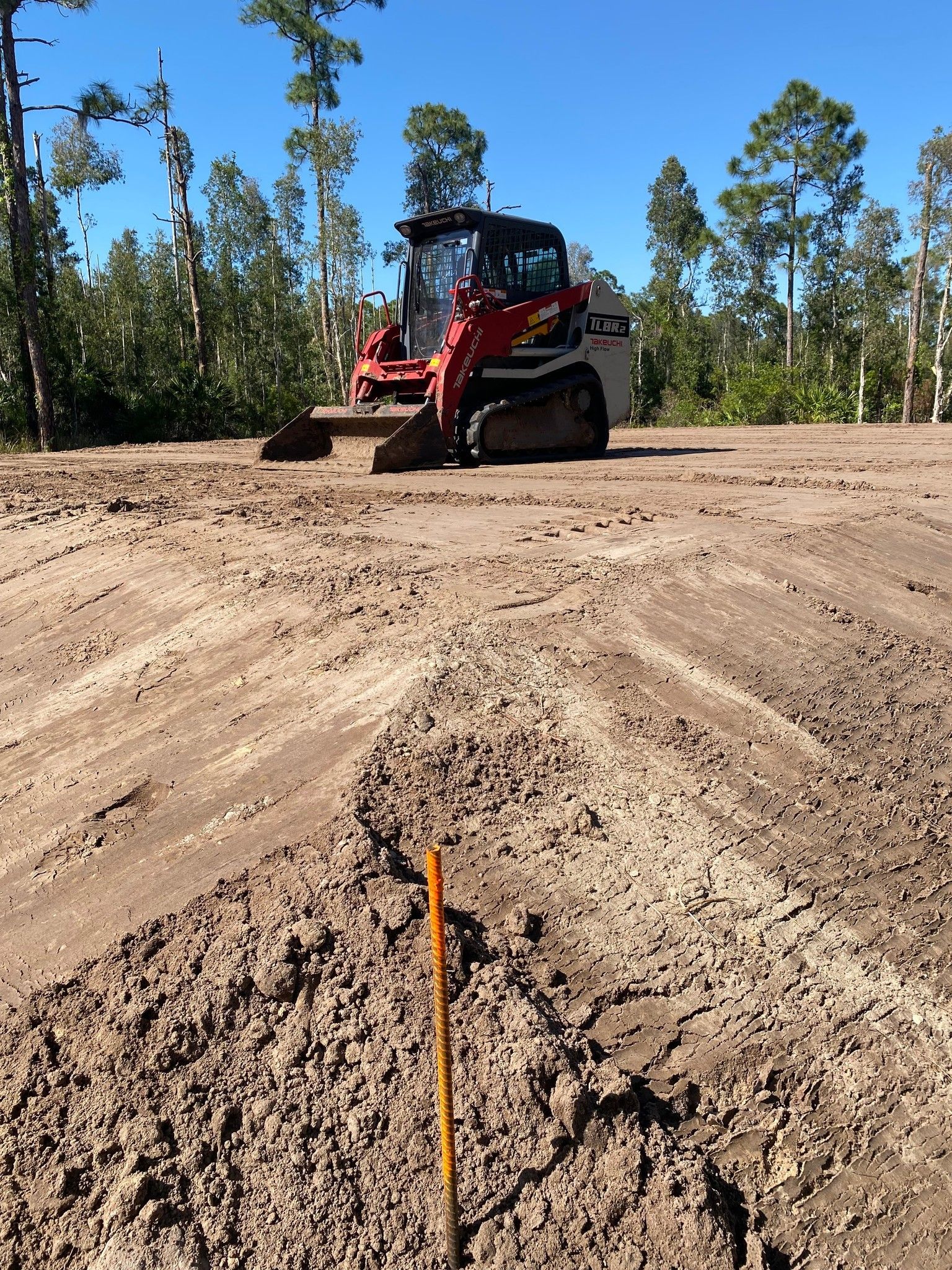 A bulldozer is driving through a dirt field with trees in the background.